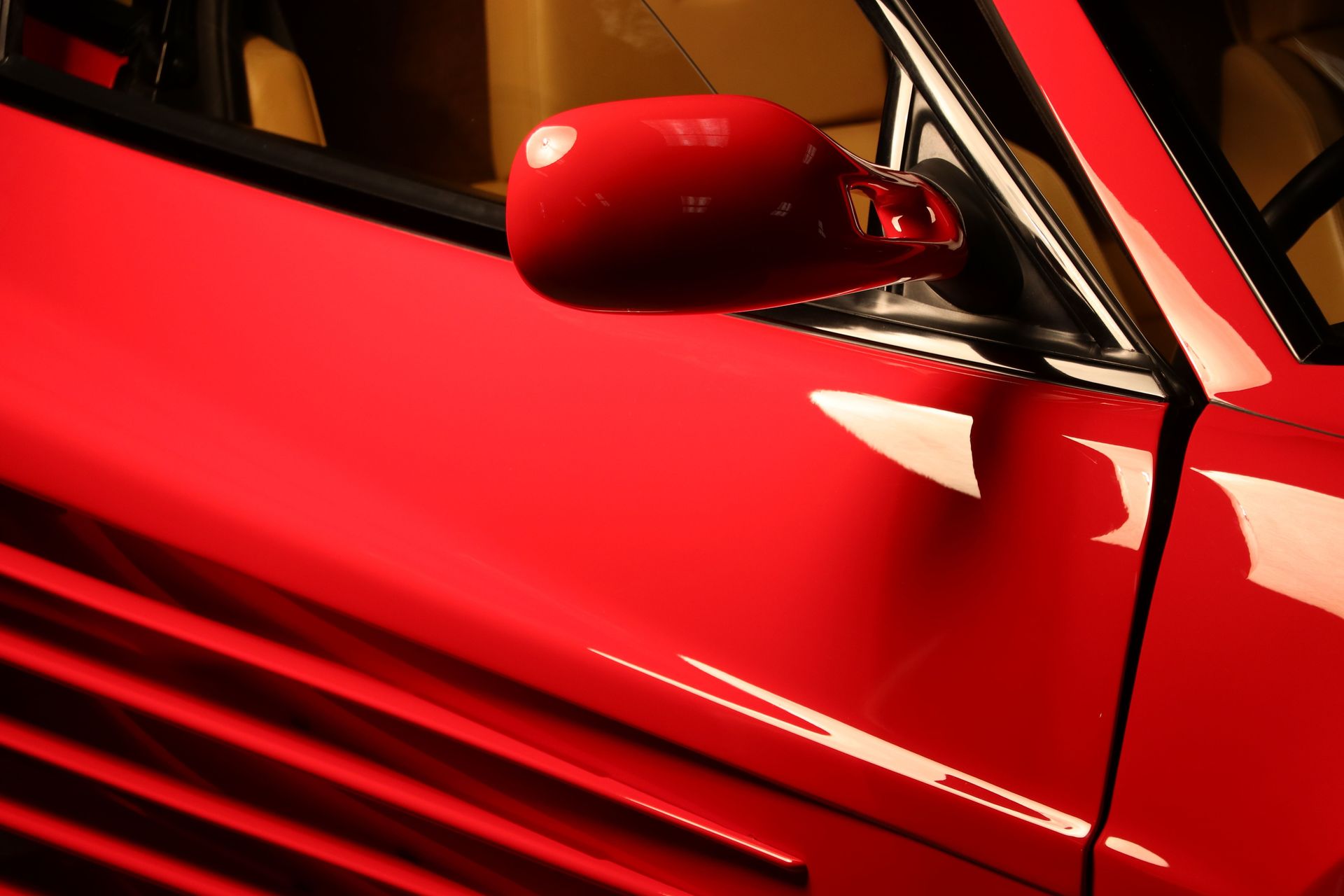 Red Ferrari Testarossa side mirror detail shot showcasing luxury design elements.